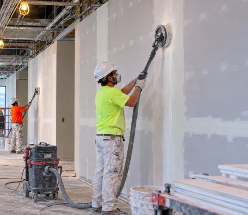 Commercial drywall crew sanding walls with dust-extraction sanders