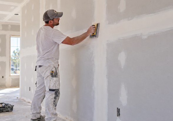 Drywall finisher hand sanding mudded joints with a sanding float